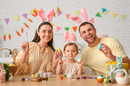 Happy family in bunny ears painting Easter eggs at home