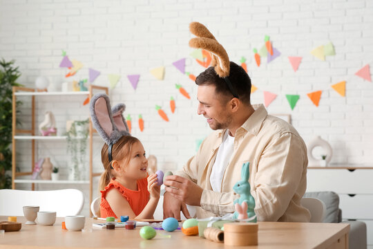 Little girl with her father in bunny ears breaking Easter eggs at home