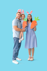 Happy family in Easter bunny ears with paper carrots on blue background