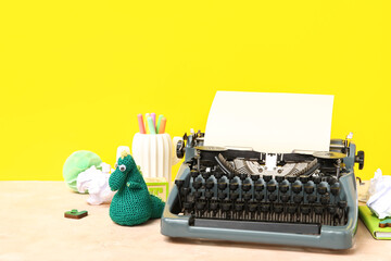 Vintage typewriter and knitted toys on table near yellow wall