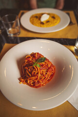 a pasta dinner at home of at a restaurant. Heaped plate of delicious Italian spaghetti pasta with fresh basil leaves and grated parmesan cheese viewed low angle from the side. 