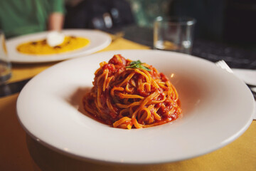 a pasta dinner at home of at a restaurant. Heaped plate of delicious Italian spaghetti pasta with fresh basil leaves and grated parmesan cheese viewed low angle from the side. 