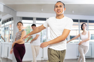 Obraz premium Happy young man and woman in sports clothes performing rock and roll dance in modern dancing room during training