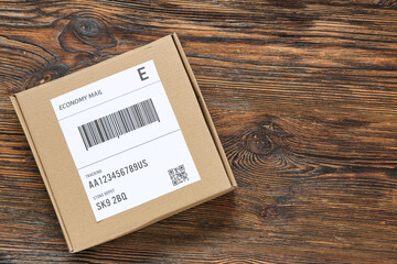 Cardboard package with label and barcode on wooden table, closeup