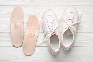 Sneakers and leather orthopedic insoles on white wooden background