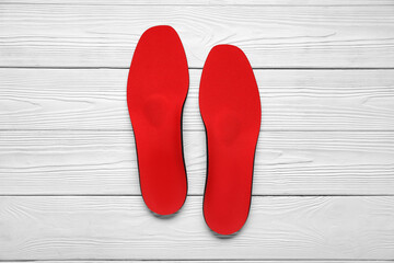 Red orthopedic insoles on white wooden background