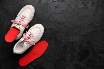 Sneakers and red orthopedic insoles on black grunge background