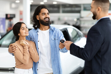 Car dealer handing keys to a happy indian couple