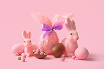 Painted and chocolate Easter eggs wrapped in paper with toy bunnies on pink background