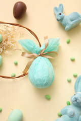 Painted and chocolate Easter eggs wrapped in paper with toy bunnies on beige background