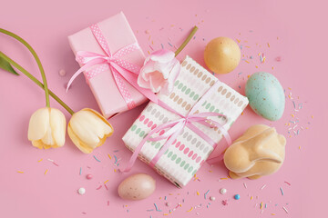 Painted Easter eggs with gift boxes, toy bunny and tulip flowers on pink background