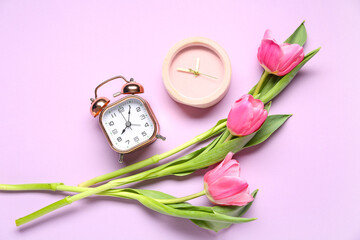 Different alarm clocks with tulip flowers on purple background