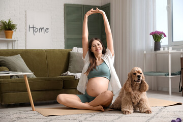 Beautiful sporty young pregnant woman with cocker spaniel stretching at home