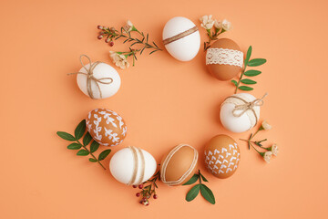 Beautiful wreath made of Easter eggs, flowers and leaves on orange background