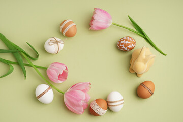 Beautiful wreath made of Easter eggs, tulip flowers and toy bunny on green background