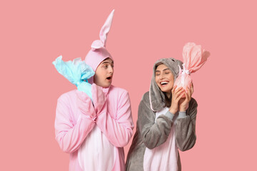 Beautiful young couple in bunny costume with Easter gift eggs on pink background
