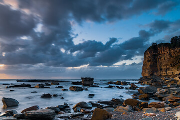Moody sunrise seascape with clouds at the rocky inlet