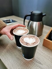 Closeup of female hand holding coffee latte with hearth shaped decorated foam on top, expresso...