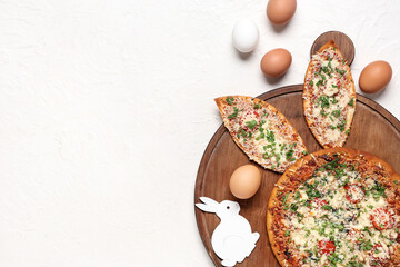 Board with tasty pizza with Easter bunny ears and eggs on white background