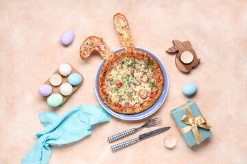 Plate with tasty pizza with Easter bunny ears, cutlery, gift box and eggs on beige grunge background