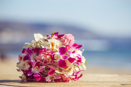 Beautiful orchid floral bridal bouquet on sandy beach with ocean background