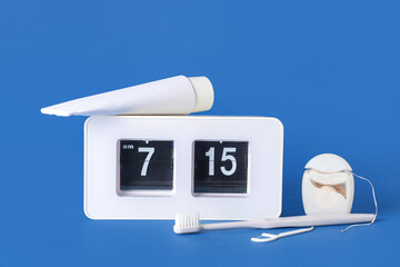 White alarm clock, dental floss toothpaste and toothbrush on blue background