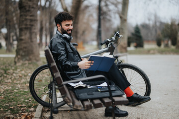 Stylish businessman enjoys working remotely from the park, using a phone and notebook with his...