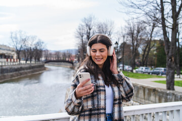 One young girl is listening to music on her wireless headphones and using her phone outdoors on a sunny day
