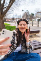 One young girl is listening to music on her wireless headphones and using her phone outdoors on a sunny day
