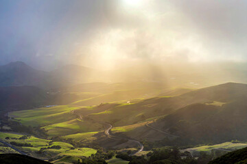 Sunbeams shine through fog to hills in spring