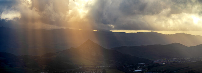 Panorama of light shining through clouds to hills, in valley