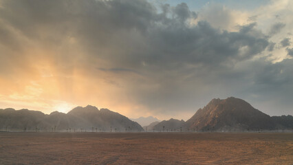 Dramatic sunset over desert landscape with mountain silhouette and cloudy sky. Scenic background.