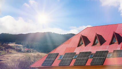Solar panels installed on red-roofed house with scenic mountain backdrop and clear blue sky with sun