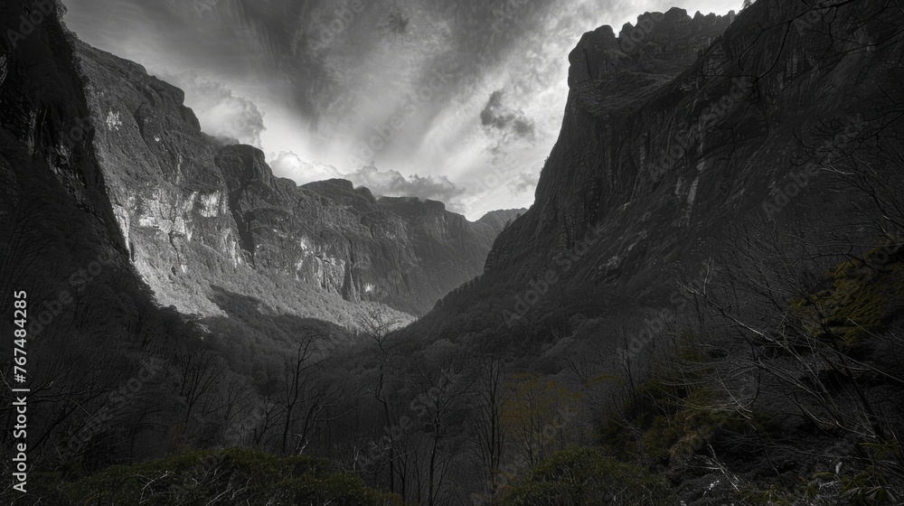 Poster a black and white photo of a mountain range with clouds in the sky and trees on the side of the moun