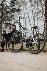 Fototapeta premium Focused businessman working remotely with his laptop and phone in a serene city park, alongside his bicycle.