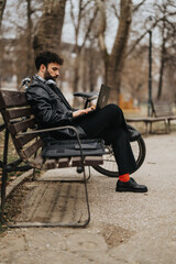 Focused male business entrepreneur uses a laptop while sitting on a park bench, exemplifying mobility and modern work style.