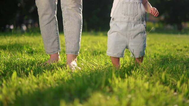 baby first steps. happy family a kid dream concept. baby walks on the grass learns to walk in the city park close-up. baby first steps in nature. mom teaches son to lifestyle walk