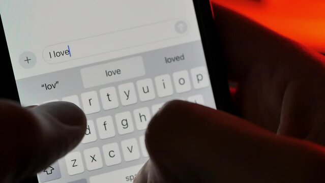 Person typing "I Love You" text message with a red heart emoji in a smartphone messenger