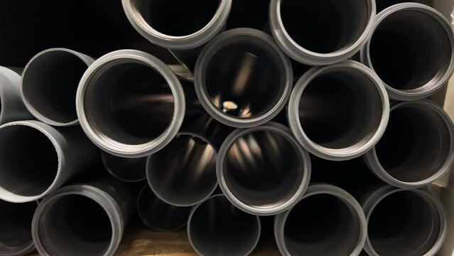 Close-up front view of a rows of plastic water pipes stacked on a shelf in a hardware store. The pipes are of different sizes, diameters. They are made of high-quality plastic