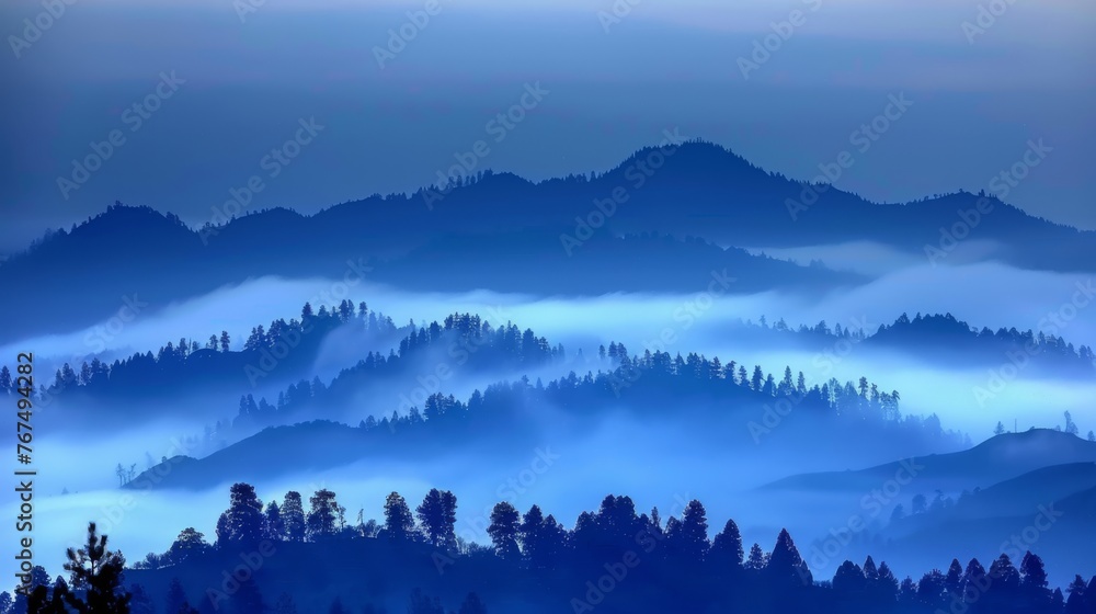 Poster a view of a foggy mountain range with pine trees in the foreground and blue sky in the background.