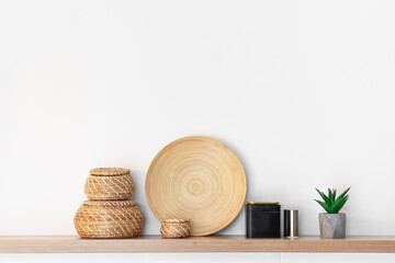 Fototapeta na wymiar Wooden shelf with woven baskets, round wooden plate, black tin, candle holder, and aloe plant against a white wall