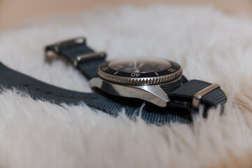 A circular watch with a gray strap on a shaggy carpet.