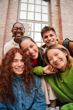Vertical portrait of a group of friends having fun and smiling together. High school students looking at camera with happy expression. Young friendly real people staring front posing for a photo