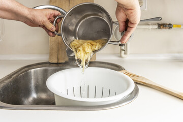 A person using a colander for freshly boiled pasta