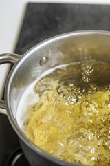 A pot of boiling water for cooking pasta on a black ceramic hob