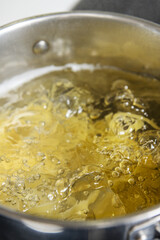 A stainless steel pot filled with boiling water for cooking pasta on a black ceramic hob