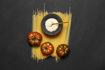 Some glossy raf tomatoes on spaghetti, grated cheese on a smooth black surface - obrazy, fototapety, plakaty