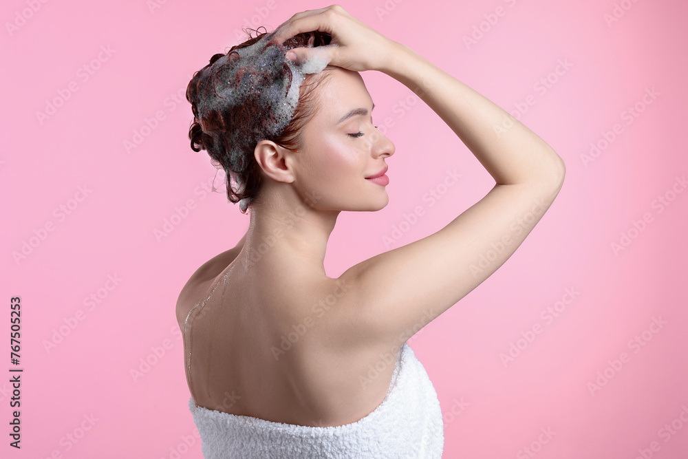 Wall mural Happy young woman washing her hair with shampoo on pink background