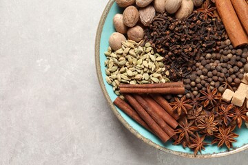 Different spices and nuts in bowl on light gray textured table, top view. Space for text