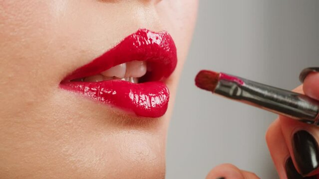 Young woman make-Up with a Red Lipstick on her lips close-up. Shooting of woman applying red lipstick. Make up routine, pink background